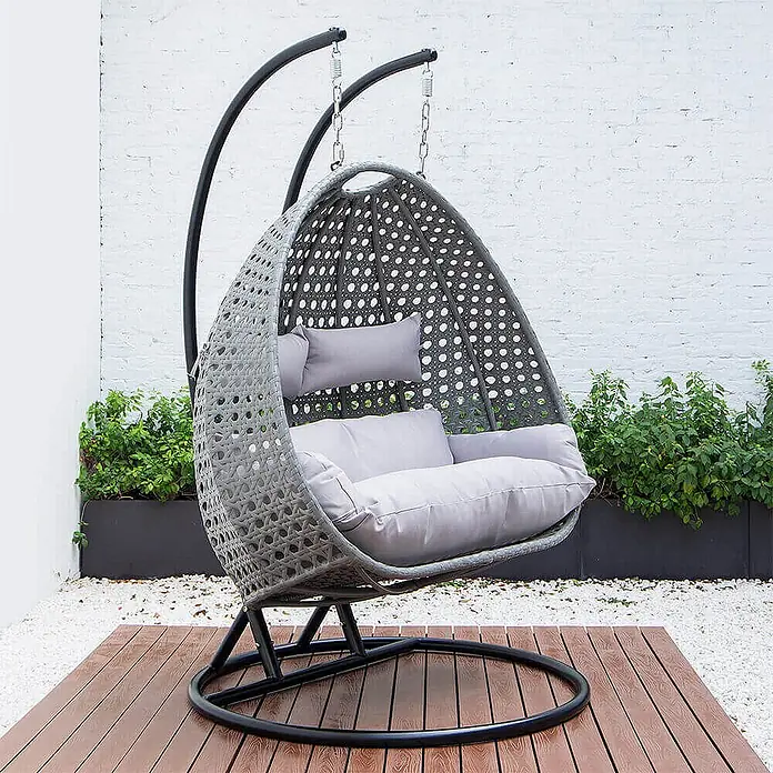 Home Deluxe Hängesessel TWIN - Kunststoff, Grau - Grauer Hänge-Eierstuhl aus Korbgeflecht mit grauen Kissen auf schwarzem Ständer auf einer Holzterrasse.