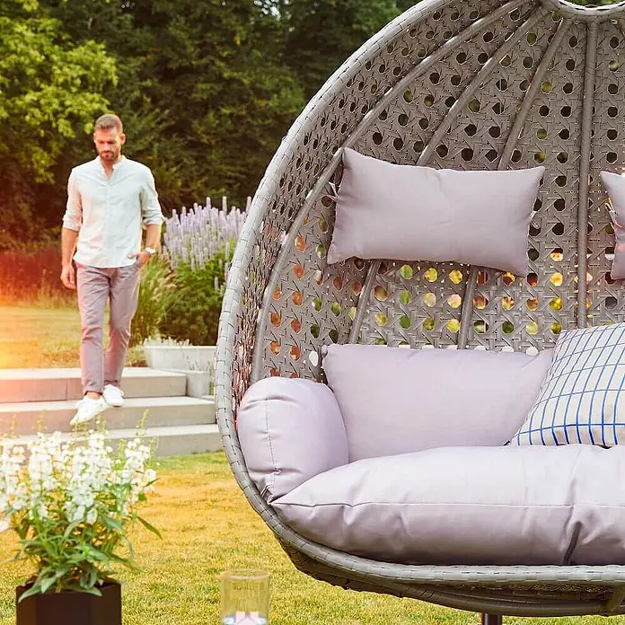 Home Deluxe Hängesessel TWIN - Kunststoff, Grau - Grauer Rattan-Hängekorb mit hellvioletten Kissen im Garten.