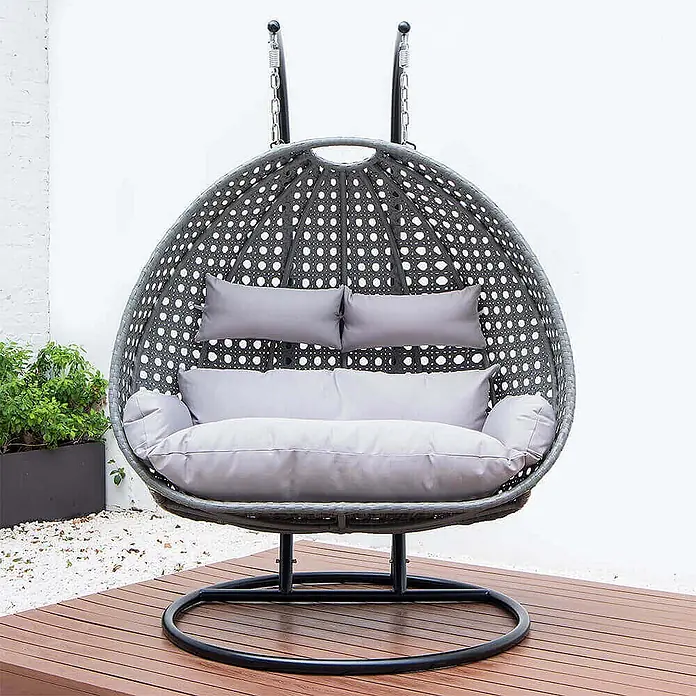 Home Deluxe Hängesessel TWIN inkl. Regenabdeckung - Kunststoff, Grau - Großer grauer Hängesessel in Rattan-Optik mit hellgrauen Kissen, auf einem dunklen Metallgestell auf einer Holzterrasse.