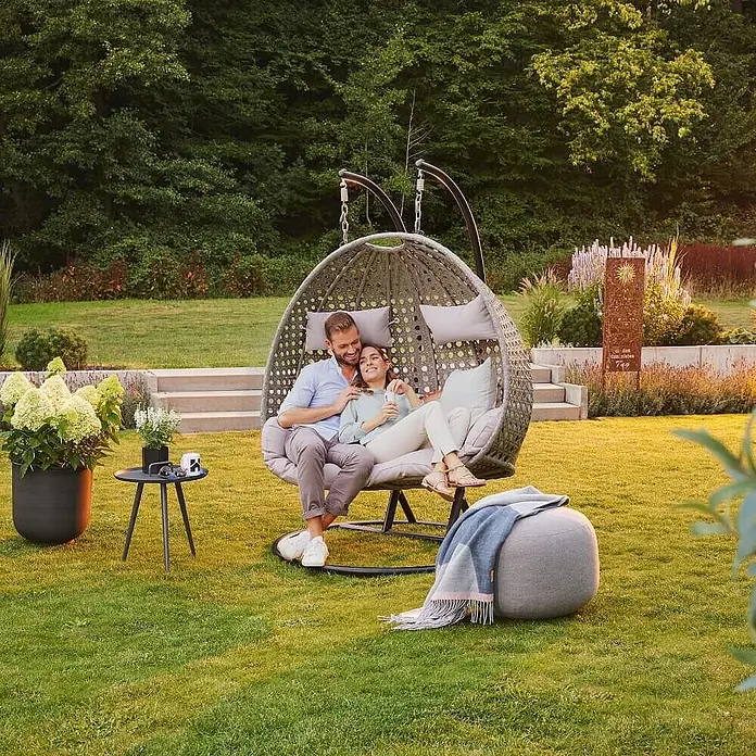 Home Deluxe Hängesessel TWIN - Kunststoff, Grau - Paar entspannt in einem grauen Doppel-Hängesessel mit hellen Kissen im Freien.