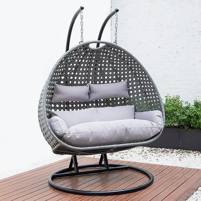 Home Deluxe Hängesessel TWIN - Kunststoff, Grau - Grauer Doppelschaukelstuhl im Ei-Design mit hellgrauen Kissen auf einer Terrasse.
