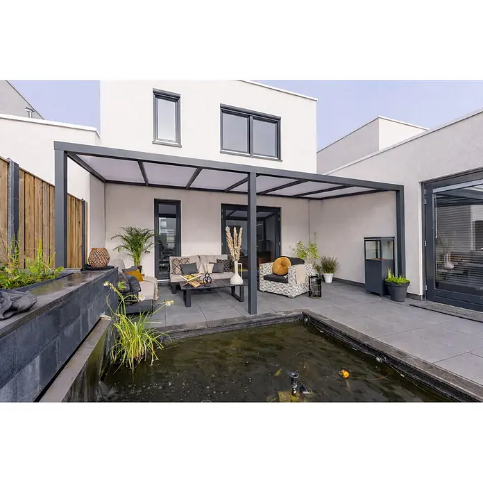 Gardendreams Terrassenüberdachung Essence - B x T: 500 x 255,5 cm, Anthrazitgrau, Polycarbonat, Opal - Eine moderne dunkelgraue Metallpergola mit lichtdurchlässigen Dachpaneelen überdacht eine Terrasse mit Sitzgelegenheiten neben einem Teich und einem modernen Haus.