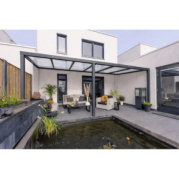 Gardendreams Terrassenüberdachung Essence - B x T: 600 x 255,5 cm, Anthrazitgrau, Verbundsicherheitsglas (VSG), Klar - Moderne dunkelgraue Aluminium-Pergola mit Glasdach über einer Außenterrasse mit Möbeln.