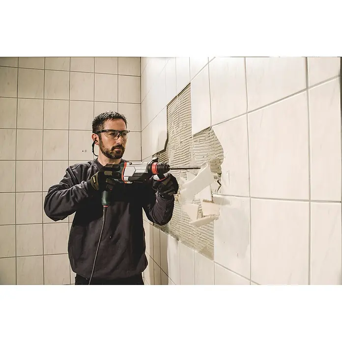 Metabo Kombihammer KHE 2860 - 880 W, 3,2 J, SDS-Plus-Aufnahme - Mann in Schutzkleidung entfernt Fliesen mit einem Bohrhammer von einer Wand.
