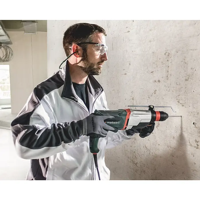 Metabo Kombihammer KHE 2860 - 880 W, 3,2 J, SDS-Plus-Aufnahme - Mann bohrt mit grün-schwarzem Metabo Bohrhammer in eine Betonwand, trägt Schutzbrille und Gehörschutz.
