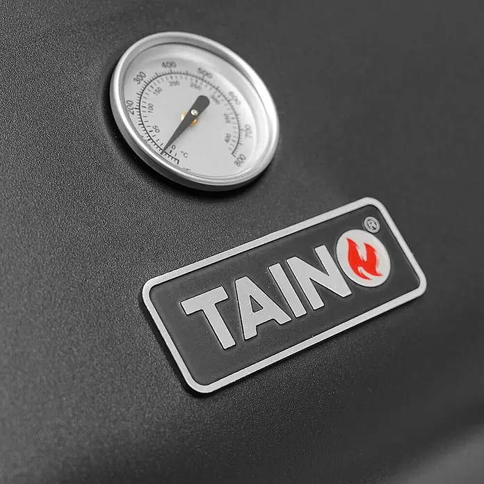 TAINO Gasgrill WABAYA 3+0 - 2,5 kW, Anzahl Brenner: 3 Stk. - Silbernes Grillthermometer und TAINO-Markenlogo mit roter Flamme auf einer schwarzen strukturierten Oberfläche.