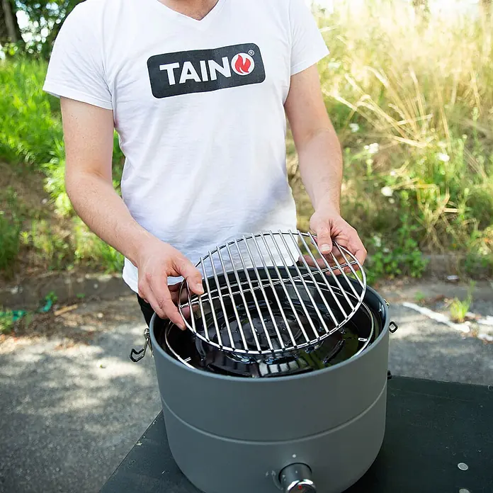 TAINO Gasgrill To-Go - 2,5 kW, Anzahl Brenner: 1 Stk. - Eine Person legt ein rundes verchromtes Grillrost in einen tragbaren grauen Grill.