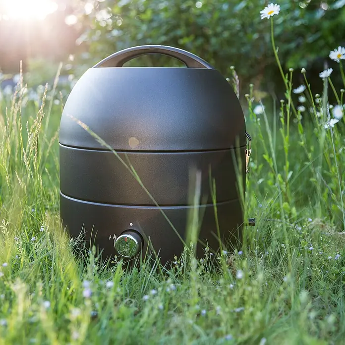 TAINO Gasgrill To-Go - 2,5 kW, Anzahl Brenner: 1 Stk. - Dunkelgrauer tragbarer Grill in hohem grünem Gras, bereit zum Kochen im Freien.