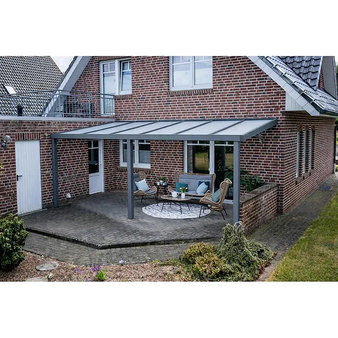 Gardendreams Terrassenüberdachung Elegance - B x T: 500 x 405,5 cm, Graualuminium, Polycarbonat, Opal - Ein graues Terrassendach mit lichtdurchlässigen Platten, das an ein Backsteinhaus angebaut ist und einen Sitzbereich im Freien schützt.