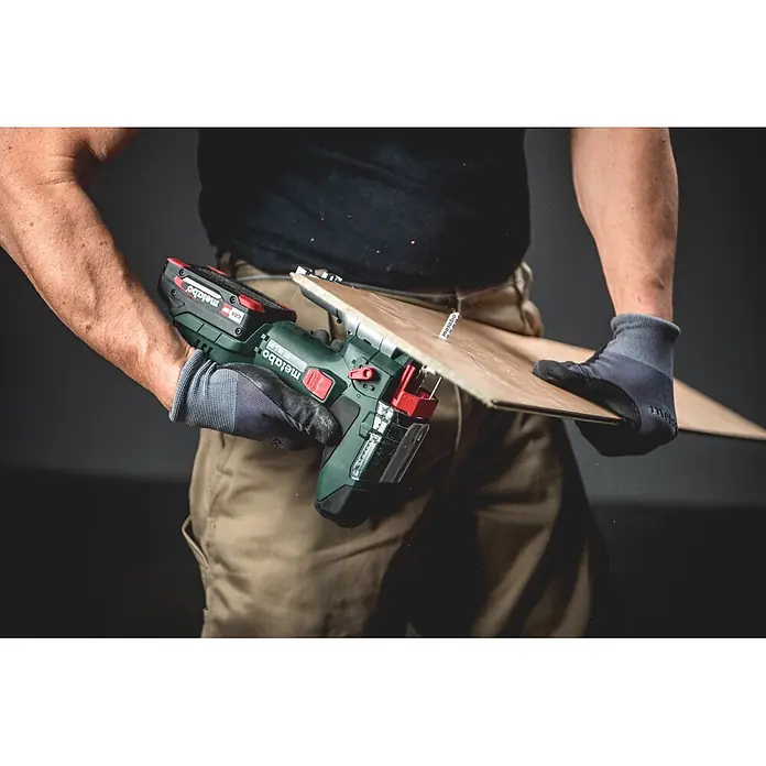 Metabo CAS 18V Akku-Pendelhubstichsäge ST 18 L 90 - 18 V, Anzahl Akkus: Ohne Akku, 750 /min - 3.000 /min - Eine Person in Arbeitshandschuhen benutzt eine grün-schwarze Metabo Akku-Stichsäge, um ein hellbraunes Holzbrett zu sägen, wobei Sägespäne entstehen.