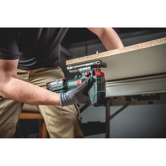 Metabo CAS 18V Akku-Pendelhubstichsäge ST 18 L 90 - 18 V, Anzahl Akkus: Ohne Akku, 750 /min - 3.000 /min - Eine Person schneidet mit einer grün-schwarzen Metabo Akku-Stichsäge und transparentem Schutz ein helles Holzbrett.