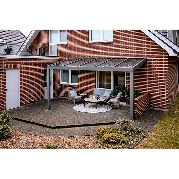 Gardendreams Terrassenüberdachung Elegance - B x T: 400 x 305,5 cm, Graualuminium, Verbundsicherheitsglas (VSG), Klar - Moderne graue Pergola mit Glasdach über gemütlicher Terrassen-Sitzgruppe mit Sofa, Stühlen und Couchtisch am Ziegelhaus.