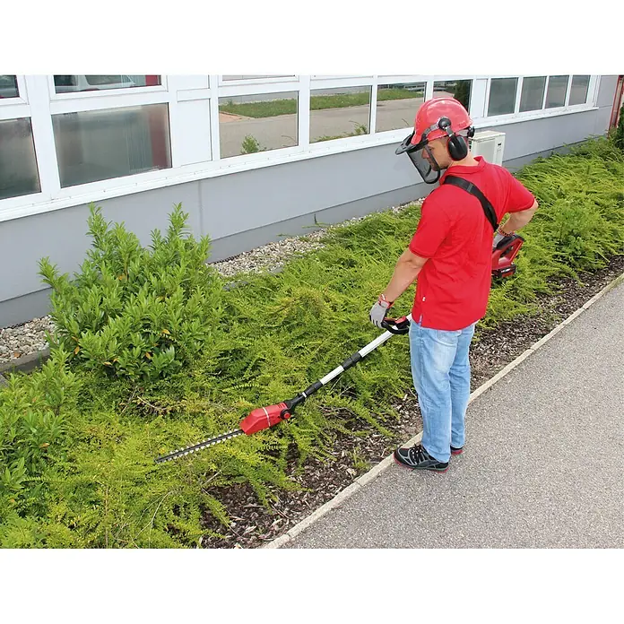 Einhell Power X-Change 18V Akku-Heckenschere GE-HH 18/45 Li T-Solo - 18 V, Li-Ionen, Ohne Akku, Schnittlänge: 40 cm - Der Mann trimmt die Hecke mit einer roten Akku-Heckenschere mit Teleskopstiel. Er trägt Schutzkleidung für die Gartenarbeit.
