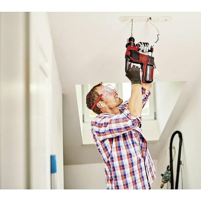 Einhell Professional PXC 18V Martillo combinado de batería Herocco - 18 V, Sin batería, 0 Ah, 2,2 J - Un hombre con gafas de seguridad usa un martillo perforador Einhell para instalar una lámpara en el techo. La herramienta es inalámbrica y potente.