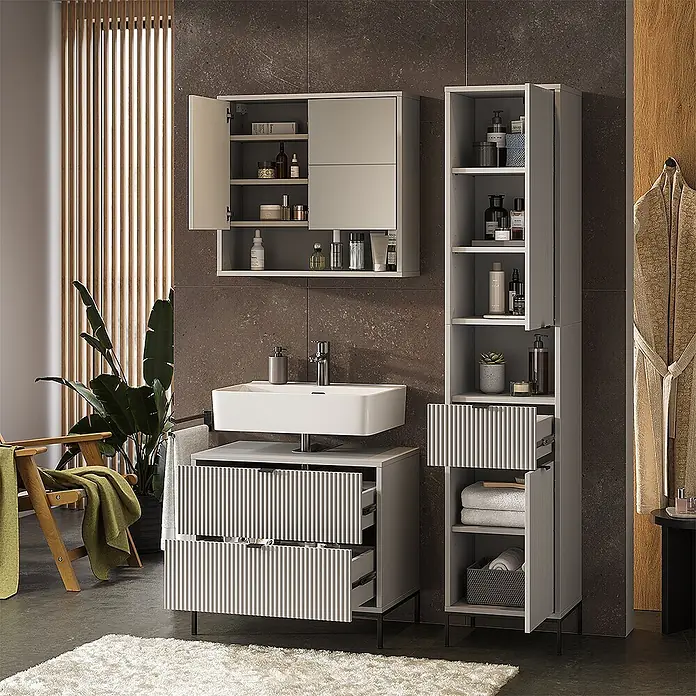 Vicco Badmöbel-Set Eliza Grau 3 Teile - Grau, Matt - Eine moderne, hellgraue Badmöbelgarnitur mit geriffelten Details, bestehend aus Wandschrank, Waschtischunterschrank und Hochschrank, gefüllt mit Pflegeprodukten und Handtüchern.