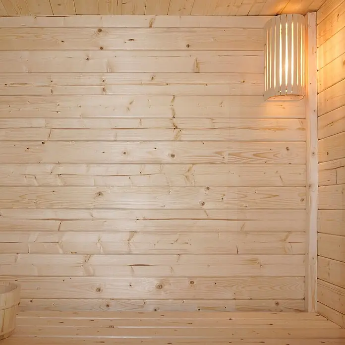 Home Deluxe Fasssauna TALO M Größe: M - Elektroofen, Holz - Helles Holzinterieur einer Sauna mit horizontalen Wandpaneelen und einer Holzlampe, die warmes Licht abstrahlt.