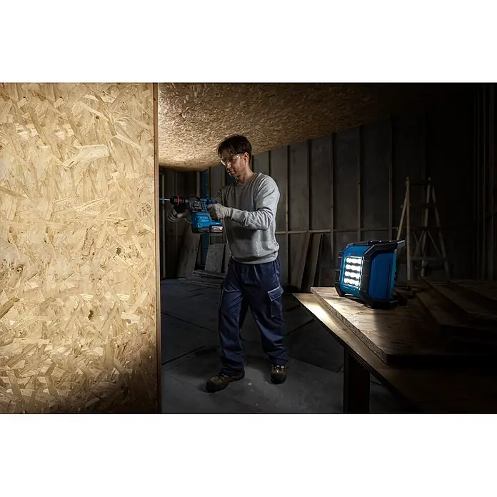 Bosch Professional AMPShare 18V LED-Akkustrahler PRO GLI18V-1500 - 18 V, Ohne Akku, 1.500 lm - Mann bohrt mit blauem Bosch Bohrhammer in OSB, beleuchtet von blauer Bosch Arbeitsleuchte im Bauraum.