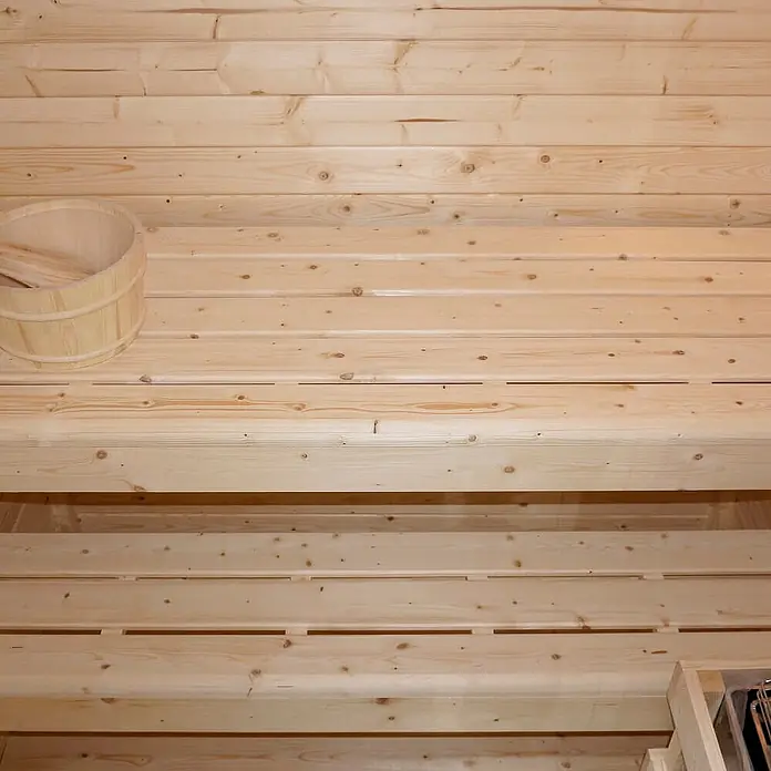 Home Deluxe Fasssauna TALO M Größe: M - Elektroofen, Holz - Heller Saunainnenraum aus Holz mit mehreren Bänken und einem Holzeimer.