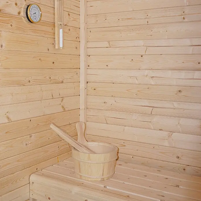 Home Deluxe Fasssauna TALO M Größe: M - Elektroofen, Holz - Helle Holzsauna mit Holzeimer, Kelle, Thermometer und Sanduhr auf einer Bank.