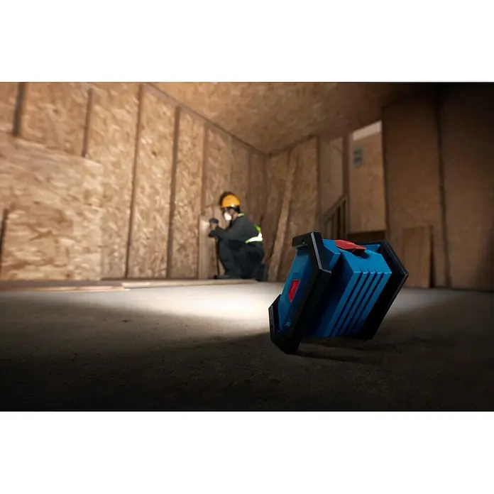 Bosch Professional AMPShare 18V LED-Akkustrahler PRO GLI18V-1500 - 18 V, Ohne Akku, 1.500 lm - Blau-schwarze Arbeitsleuchte, die einen Bauarbeiter beleuchtet. Die Lampe liegt auf dem Boden und wirft einen hellen Strahl.