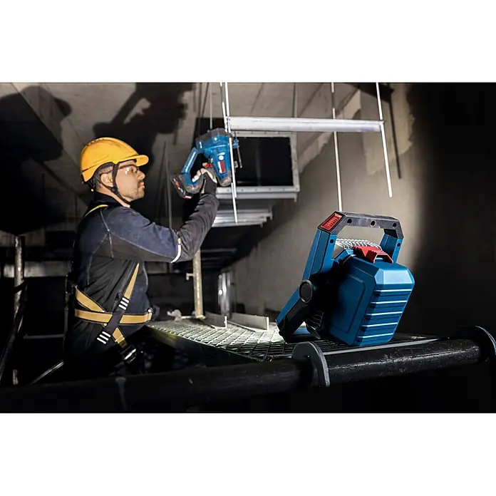 Bosch Professional AMPShare 18V LED-Akkustrahler PRO GLI18V-3000 - 18 V, Ohne Akku, Lichtstrom: 3.000 lm - Blaue und schwarze Arbeitsleuchte auf Gerüst, beleuchtet Bauarbeiter bei der Nutzung eines Elektrowerkzeugs.