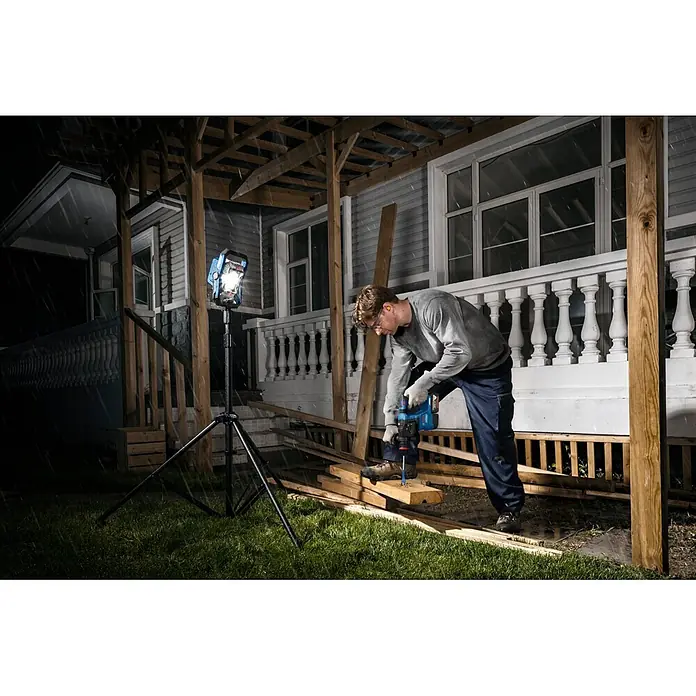Bosch Professional AMPShare 18V LED-Akkustrahler PRO GLI18V-3000 - 18 V, Ohne Akku, Lichtstrom: 3.000 lm - Blaue und schwarze Arbeitsleuchte auf Stativ beleuchtet einen Mann, der nachts im Freien Holz bohrt.