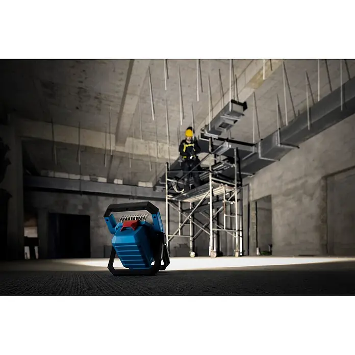 Bosch Professional AMPShare 18V LED-Akkustrahler PRO GLI18V-3000 - 18 V, Ohne Akku, Lichtstrom: 3.000 lm - Blau-schwarze Arbeitsleuchte, die eine Baustelle mit einem Arbeiter auf einem Gerüst beleuchtet.