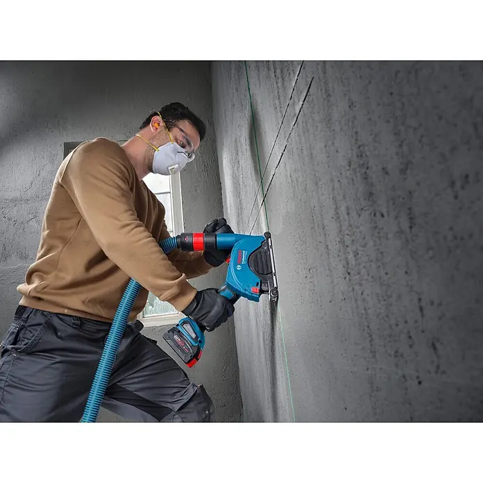 Bosch Professional AMPShare 18V Akku-Winkelschleifer PRO GWS18V-11PS - 18 V, Ohne Akku, Durchmesser Scheibe: 125 mm - Eine Person nutzt eine blaue Bosch Mauernutfräse mit Staubabsaugung, um Linien in Beton zu schneiden, mit Schutzausrüstung.