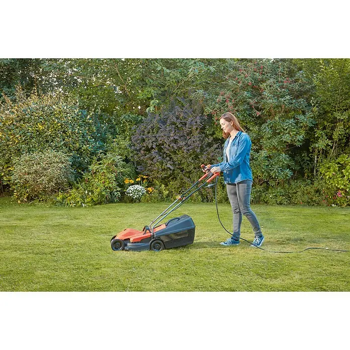 Black+Decker Cortacésped eléctrico BEMW451BH-QS - 1.200 W, Ancho de corte: 32 cm - Mujer usando una cortadora de césped para cortar el césped. La cortadora de césped es naranja con un recogedor de hierba negro.