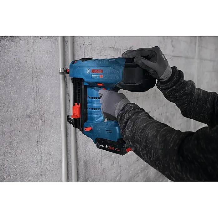 Bosch Professional Kabelhalter Pro EMD - 6 mm, 100 Stk. - Person in Handschuhen nutzt blauen und schwarzen Bosch Akku-Nagler (GNB 18V-40) an Betonwand neben Rohren.