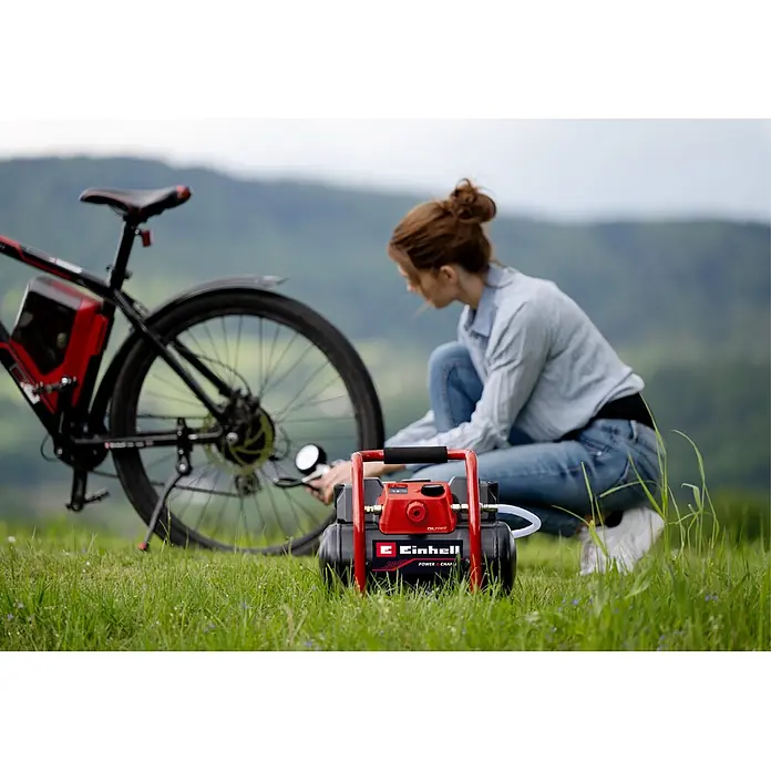 Einhell Power X-Change 18V Akku-Kompressor TE- AC 36/150 Li OF-Solo - 36 V, Ohne Akku, 8 bar - Roter und schwarzer Einhell-Kompressor füllt draußen einen Fahrradreifen auf, eine Person kniet im Gras.