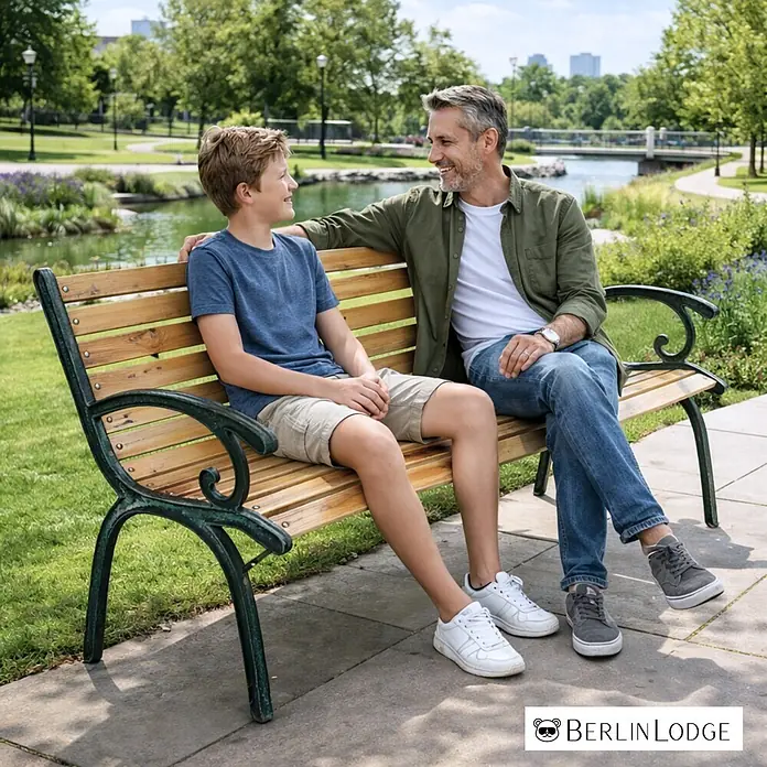 Berlinlodge Gartenbank MADEIRA 2-Sitzer - Lackiert|Pulverbeschichtet, Natur - Hölzerne Parkbank mit dunklem Metallgestell, von zwei Personen in einem sonnigen Park genutzt.