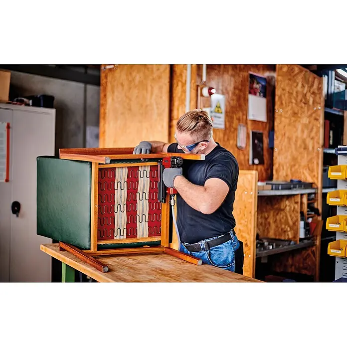 Einhell Flüsterkompressor TE-AC 135/24 Silent Plus - 750 W, Max. Druck: 8 bar, 24 l - Mann benutzt roten und schwarzen Drucklufttacker an Stuhlpolsterung.
