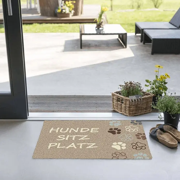 Akzente Fußmatte Feel - 70 x 50 cm, Mehrfarbig, Motiv / Muster|Tiere|Schriftzug - Beige Fußmatte mit "HUNDE SITZ PLATZ" Schriftzug und bunten Pfotenabdrücken vor einem Terrasseneingang.