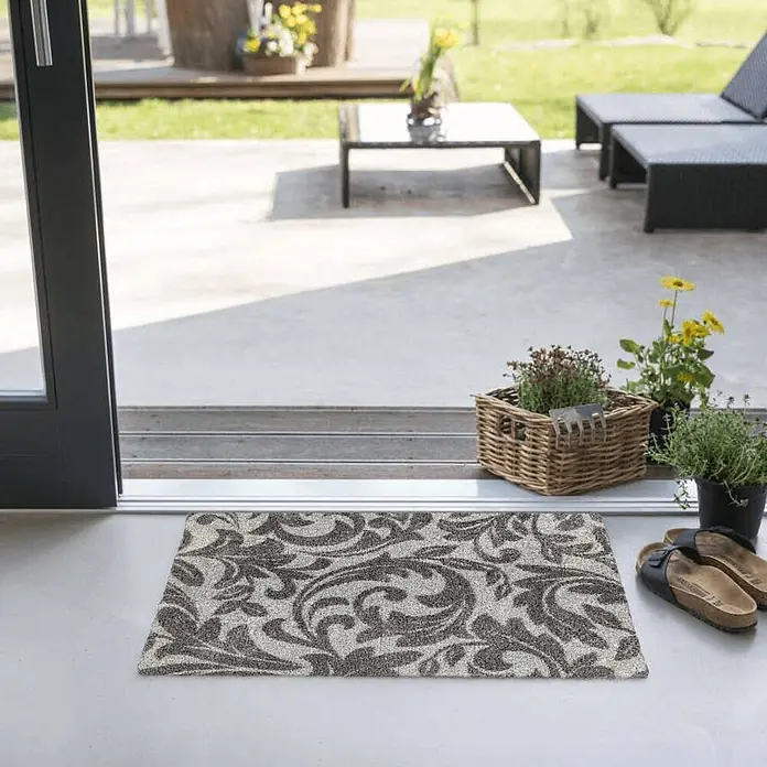 Akzente Fußmatte Feel - Mehrfarbig, Motiv / Muster|Floral - Grau-beige gemusterte Fußmatte am Eingang, führt zu einer Außenterrasse mit Möbeln.