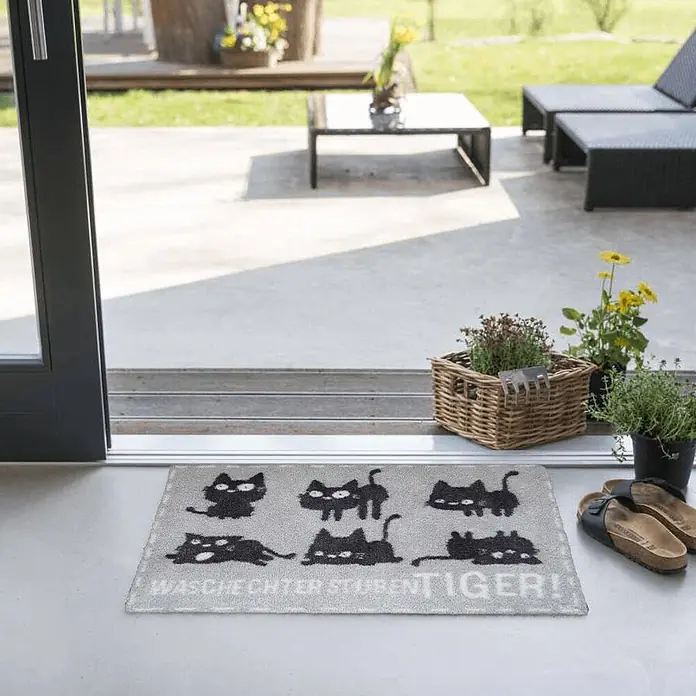 Akzente Fußmatte Feel - Mehrfarbig, Tiere|Schriftzug - Graue Fußmatte mit schwarzen Katzenmotiven und Text, platziert vor einer Terrassentür.