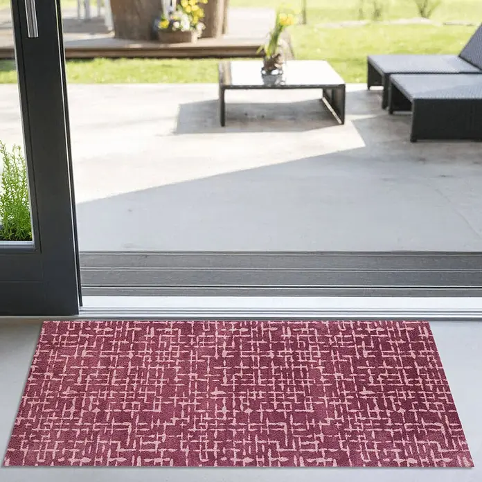 Akzente Fußmatte Feel - 200 x 80 cm, Mehrfarbig, Motiv / Muster - Ein rechteckiger burgunderroter Fußabtreter mit hellem, abstraktem Muster liegt an der Schwelle einer Terrassentür zu einem Sitzbereich im Freien.