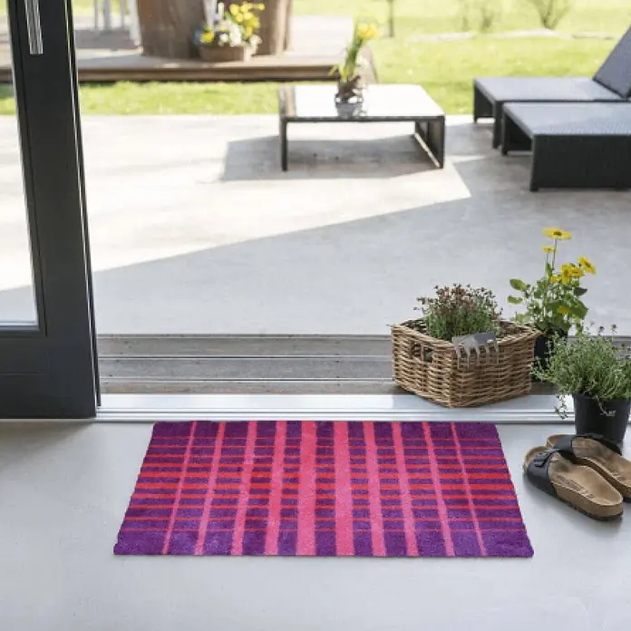Akzente Fußmatte Feel - Mehrfarbig, Motiv / Muster - Lila- und magentafarbene gestreifte Fußmatte vor einer Tür, die zu einer Terrasse führt.