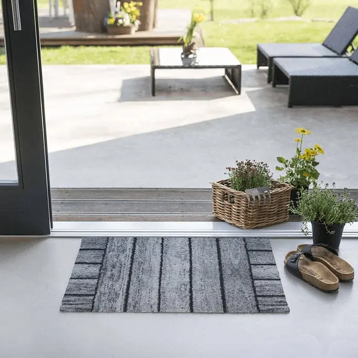 Akzente Fußmatte Feel - Mehrfarbig, Holz-Optik - Grau-schwarze Fußmatte mit Holzplankenmuster, an einem Terrasseneingang platziert.