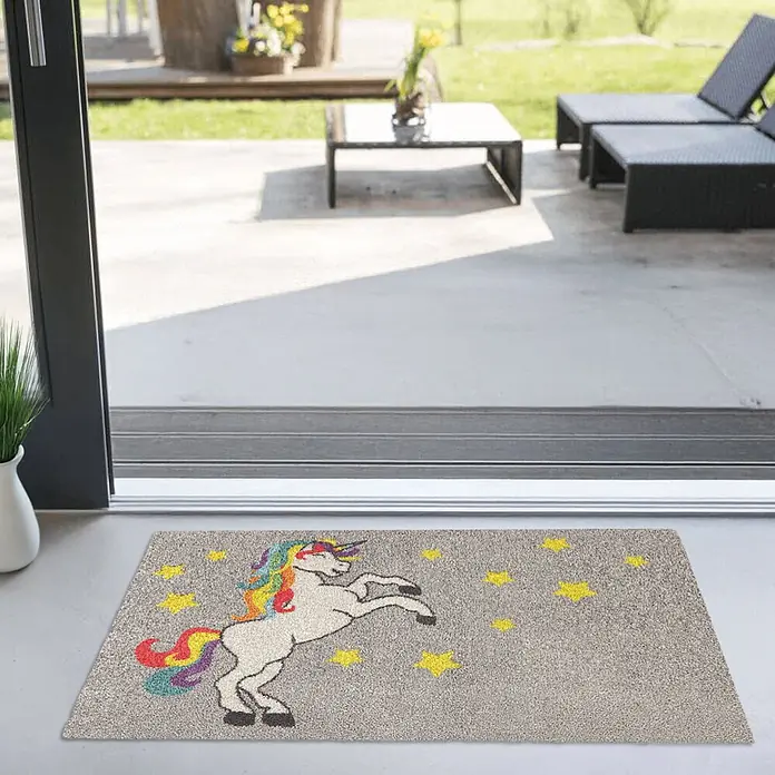Akzente Fußmatte Feel - 100 x 70 cm, Mehrfarbig, Motiv / Muster|Tiere - Eine strukturierte graue Fußmatte mit einem weißen Einhorn, Regenbogenmähne und gelben Sternen vor einem Außeneingang.
