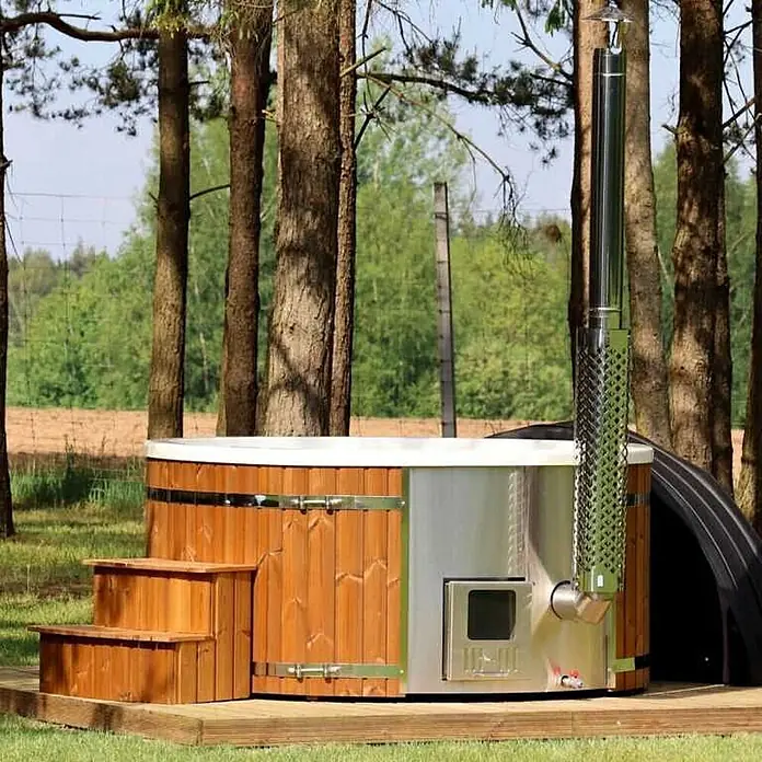 Loocone Hot Tub Hot Tub Acryl 200 cm V4A Holzofen - 200 cm, Max. Personenzahl: 5 Stk. - Holzbeheizter Whirlpool mit Holzverkleidung, Edelstahl-Ofen und hohem Schornstein auf einer Holzterrasse im Grünen.