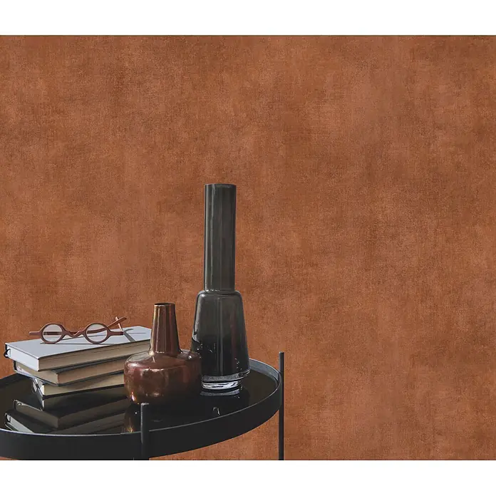 Papel pintado Texturado - Rojo arcilla, 10 x 0,53 m - Una mesa auxiliar negra con tapa de cristal sostiene libros, gafas y dos jarrones, frente a una pared marrón texturizada.