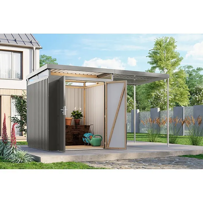 Karibu Gerätehaus Aurum 2 mit Anbaudach - Außenmaß inkl. Dachüberstand (B x T): 420 x 215 cm, Metall, Graualuminium - Ein dunkelgrauer Geräteschuppen aus Metall mit offener Tür zeigt Gartenwerkzeuge. Ein integrierter Carport erstreckt sich vom Schuppen in einem modernen Garten.