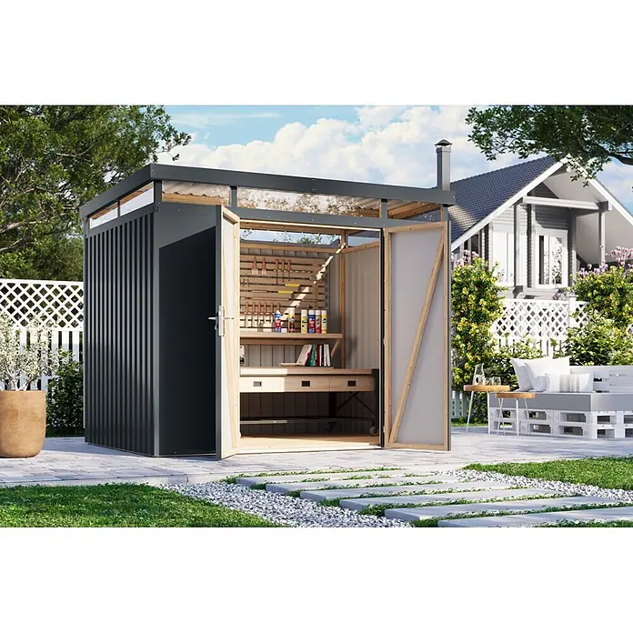 Karibu Gerätehaus Aurum 3 - Außenmaß inkl. Dachüberstand (B x T): 298 x 215 cm, Metall, Anthrazit - Dunkelgrauer Gartenschuppen mit offenen Türen, der eine helle Holzwerkbank und Werkzeuge in einem üppigen Garten zeigt.