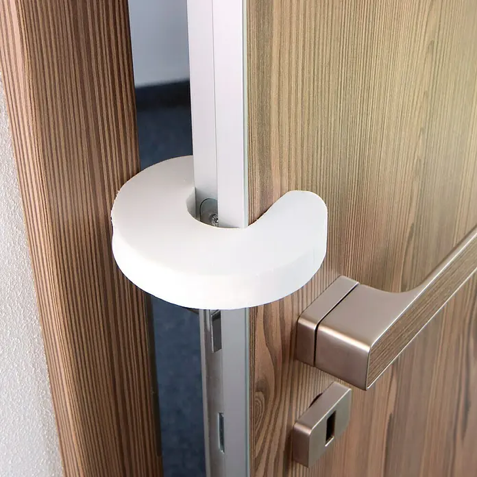 Tür- & Fensterstopper - L x B x H: 85 x 95 x 7 mm, Material: Kunststoff, Weiß - Nahaufnahme eines Türschutzes aus Schaumstoff, der an einer Tür angebracht ist, um das Einklemmen von Fingern zu verhindern.