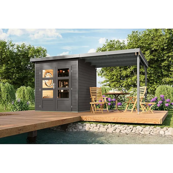 Karibu Gartenhaus Pluto 1 B - Außenmaß inkl. Dachüberstand (B x T): 447 x 228 cm, Holz, Terragrau/Grau - Dunkelgraues Gartenhaus mit angehängter Pergola, Holzterrasse und Gartenmöbeln am Teich.
