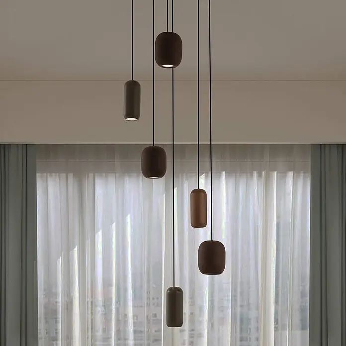 Lucande Pendelleuchte Narion - L x B x H: 40 x 40 x 150 cm, Multicolour, Schwarz matt, dunkelGrün matt, braun matt, GU10 - Mehrere dunkle Pendelleuchten in Braun und Grau in verschiedenen Formen, beleuchtet, hängen über Vorhängen von der Decke.