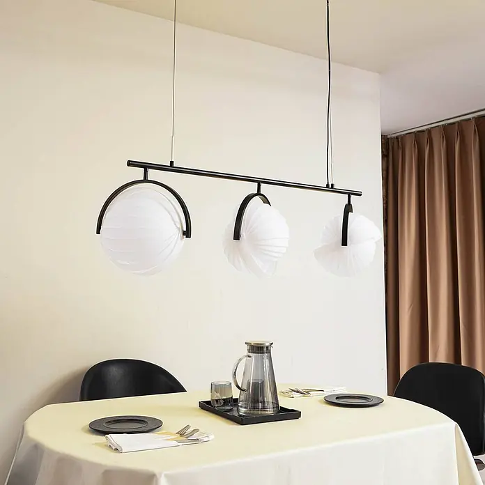 Lucande Pendelleuchte Helva - L x B x H: 120 x 32 x 27 cm, weiß / opal, weiß, Schwarz, E27 - Lineare Pendelleuchte mit drei weißen plissierten Kugelschirmen und schwarzem Metallrahmen über einem Esstisch.