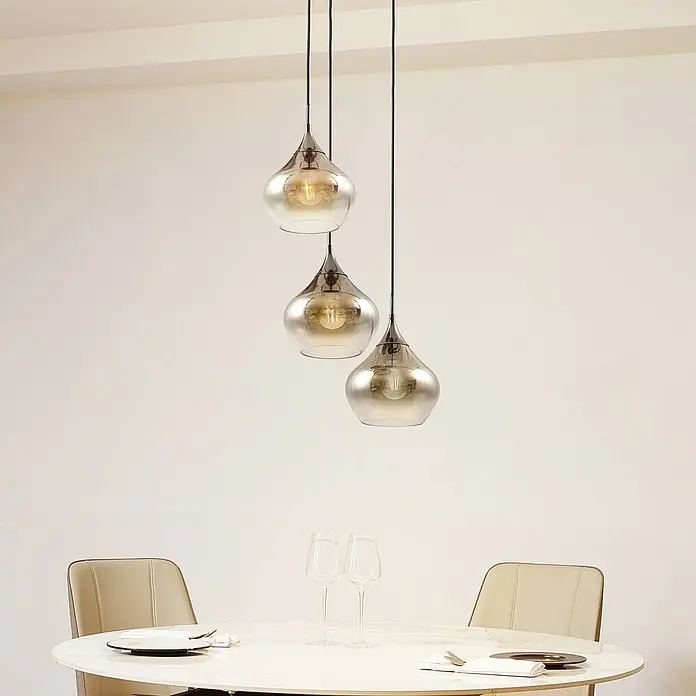 Lucande Pendelleuchte Jarven - L x B x H: 44 x 44 x 17,5 cm, alu / grau / zink, rauchgrau, Schwarz, E27 - Drei tropfenförmige Pendelleuchten aus Rauchglas mit Metallaufsätzen hängen über einem weißen Esstisch.