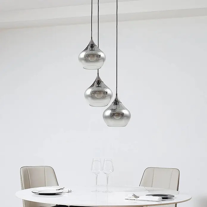 Lucande Pendelleuchte Jarven - L x B x H: 44 x 44 x 17,5 cm, alu / grau / zink, rauchgrau, Schwarz, E27 - Drei rauchgraue Glaspendelleuchten hängen über einem weißen Esstisch mit Stühlen und zeigen ein modernes Esszimmer.
